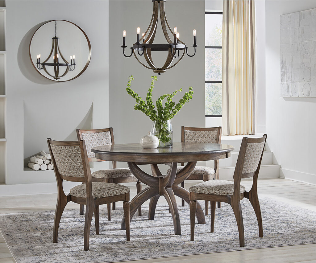 Dining room furniture with round table, upholstered chairs, chandelier, and greenery centerpiece
